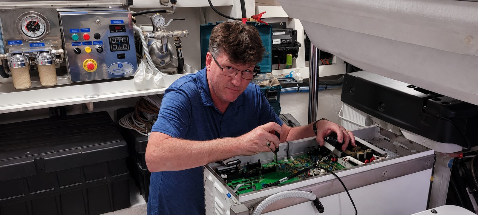 Technician servicing an open onboard electronic control system in a yacht machinery space.