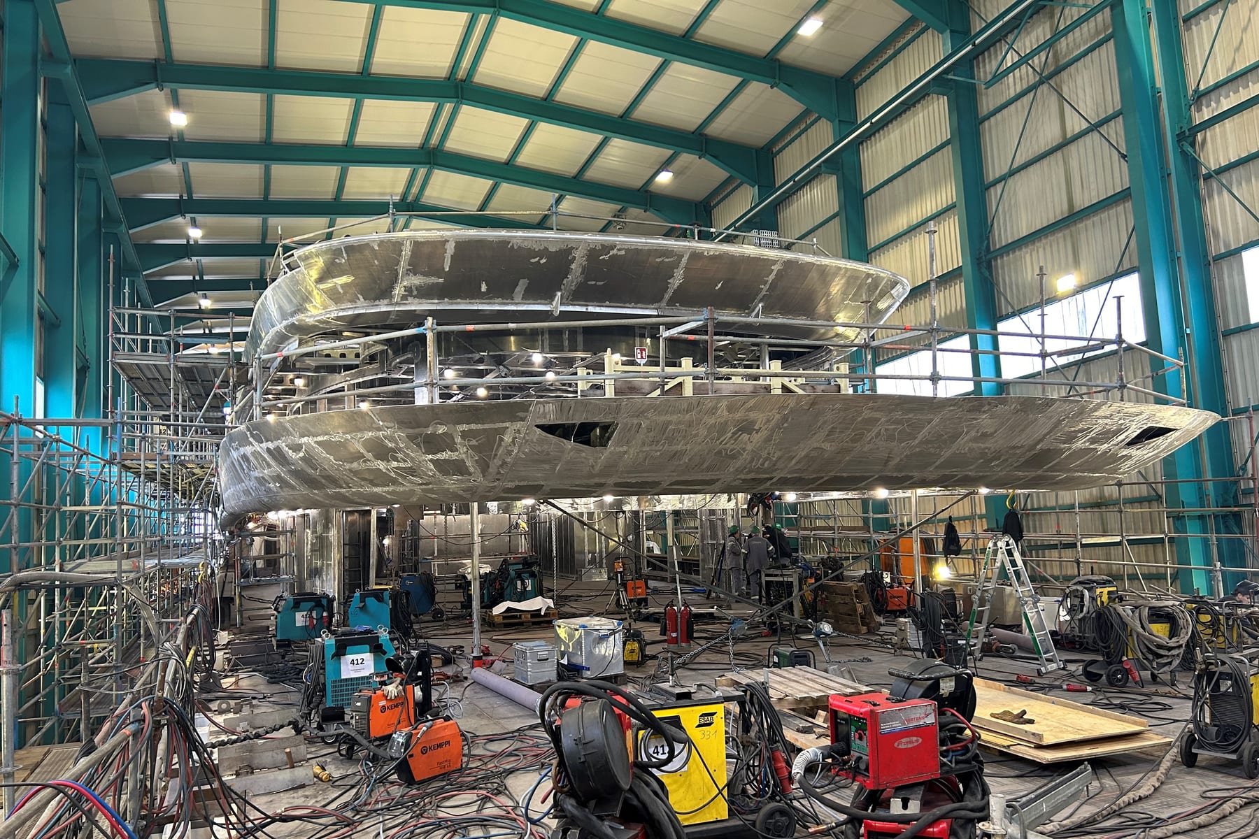 Aluminum superyacht hull in a build shed surrounded by welding equipment