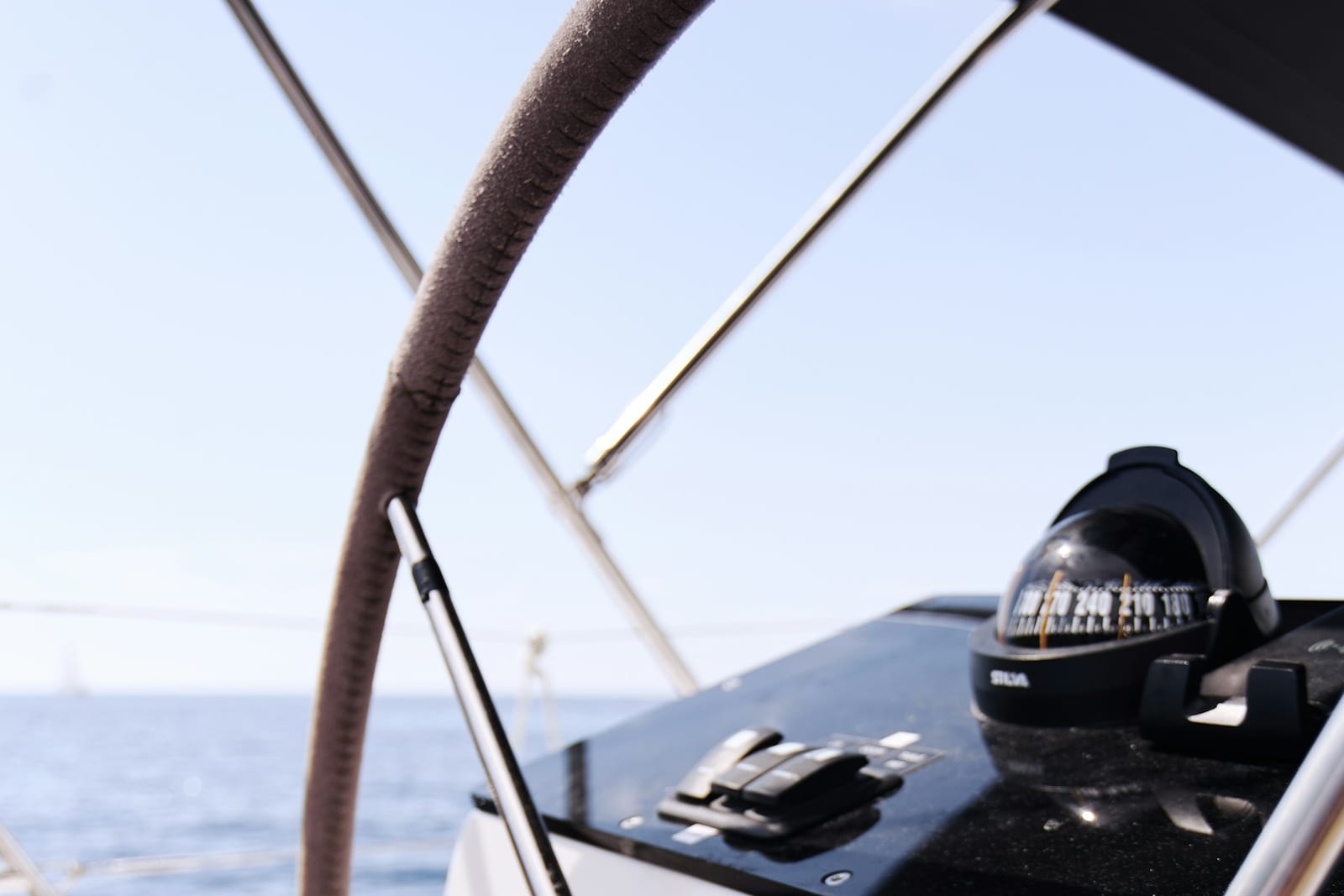 Sailing yacht helm with wheel and steering compass under way in open water.